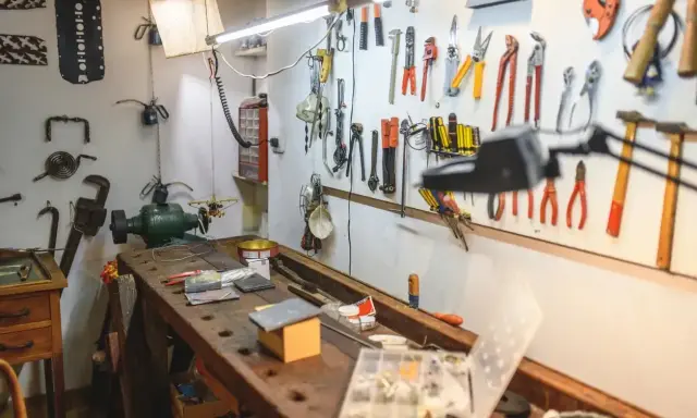 Warsztat domowy pełen narzędzi i pomysłów na majsterkowanie. Widać tu imadło, szlifierkę, mnóstwo kluczy, śrubokrętów i innych przyrządów.