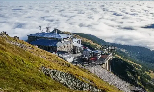 Widok na Kasprowy Wierch szlak z kolejką linową i budynkami, nad morzem chmur.