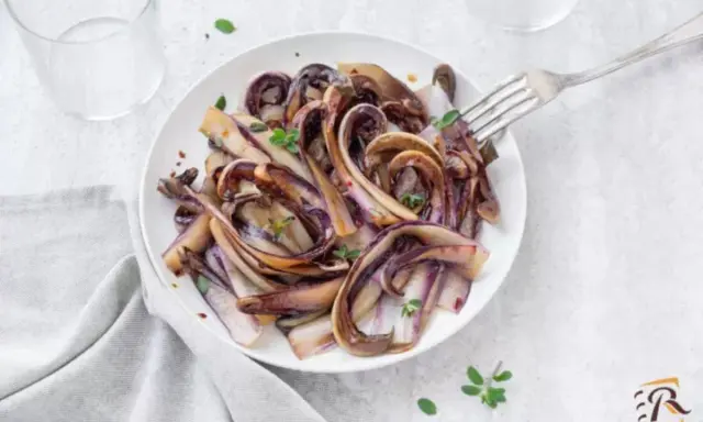 Radicchio in padella, caramellato e profumato, servito su un piatto bianco con un tocco di erbe aromatiche.