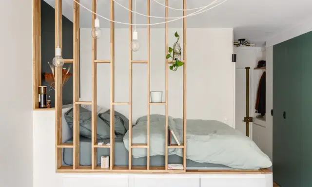 Aménagement astucieux d'un studio T2 avec un lit douillet séparé par une étagère en bois.