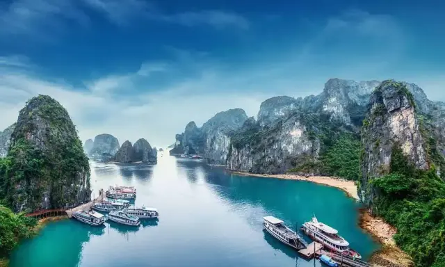 Widok na Zatokę Ha Long, kiedy do Wietnamu. Statki cumują przy turkusowej wodzie, otoczone wapiennymi wyspami porośniętymi zielenią.