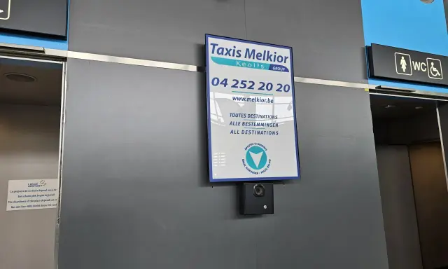 Taxi Melkior-skylt vid lgg flygplats. En övervakningskamera är monterad under skylten.