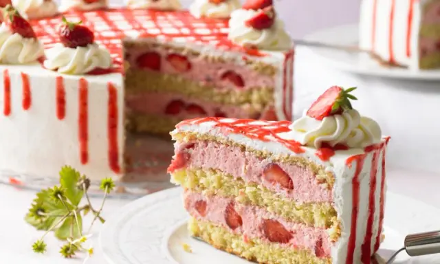 Eine moderne Erdbeertorte mit drei Schichten Biskuit, Erdbeercreme und frischen Erdbeeren, verziert mit Sahnetupfern und rotem Zuckerguss.