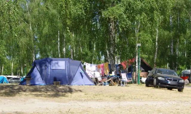Idealne miejsce, gdzie pod namiot nad jezioro. W tle las, a przed namiotem rozłożone krzesła i suszące się pranie.