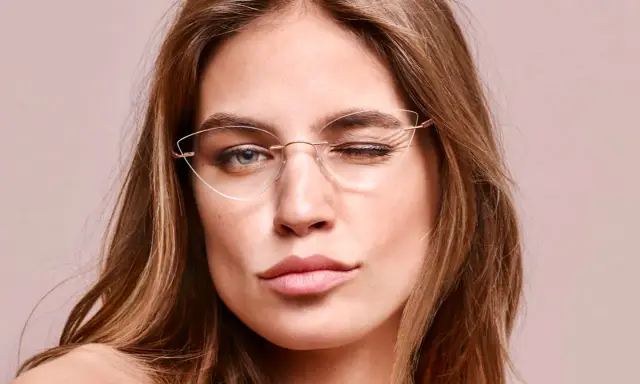 Eleganckie okulary korekcyjne bez oprawek podkreślają spojrzenie kobiety, która mruga do obiektywu.