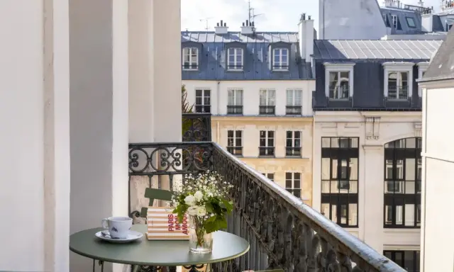Petit-déjeuner sur le balcon avec vue sur les toits de Paris. Une tasse de café, un livre "Paris mon amour" et des fleurs, un moment de détente au saint-grégoire.