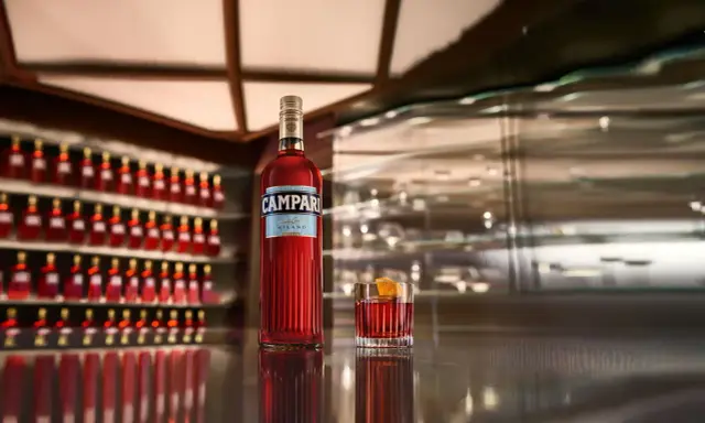 Eine Flasche Campari und ein Glas mit dem roten Aperitif stehen auf einer glänzenden Theke. Die Frage "wie schmeckt Campari?" wird durch den Anblick des ikonischen Getränks aufgeworfen.