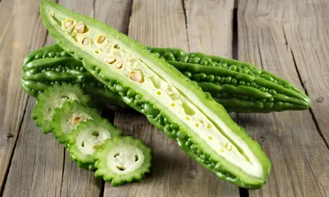 A halved bitter melon plant reveals its seedy interior, with sliced rounds fanned out on a rustic wooden surface.