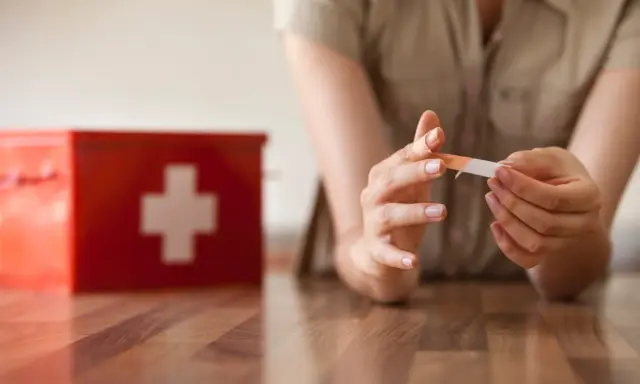 Une personne applique un pansement sur son doigt, près d'une trousse de secours rouge. L'objectif est une cicatrisation rapide.