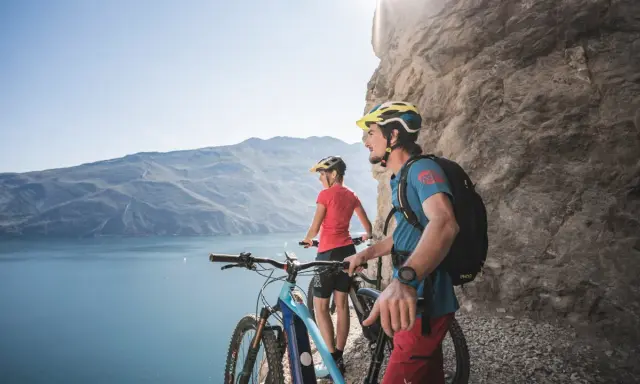 Ein Paar genießt die Aussicht auf den Gardasee während einer E-Bike-Tour. Die Berge und das klare Wasser bilden eine atemberaubende Kulisse.