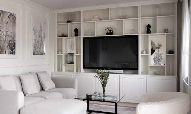 Vitt, platsbyggt bokhyllesystem i vardagsrummet med TV, soffa och dekorationer.