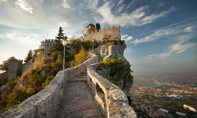 Sentiero in pietra che sale verso le fortificazioni di San Marino città, con vista panoramica sulla valle sottostante.