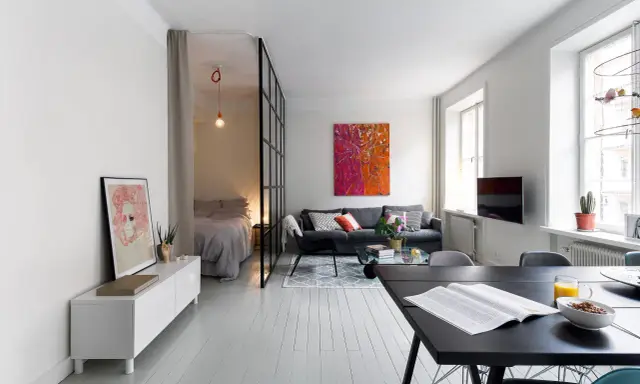 Smart lösning för att bo på liten yta. Sovrummet avskiljs med en glasvägg. Vardagsrummet har en soffa och ett soffbord.