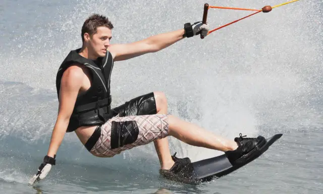 Młody mężczyzna na desce, ciągnięty przez linę, pokazuje, **wakeboarding co to** jest – sport wodny pełen adrenaliny i zabawy.