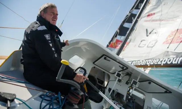 Un homme expérimenté, kito de pavant, tient la barre d'un voilier, concentré sur la course.