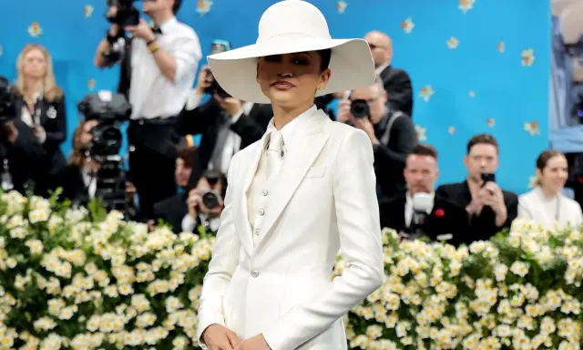 Zendaya, deslumbrante con traje blanco y sombrero, posa ante cámaras y flores.