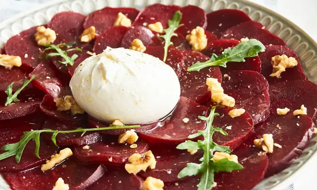 Rote Bete Carpaccio mit Burrata, Walnüssen und Rucola auf einem Teller.