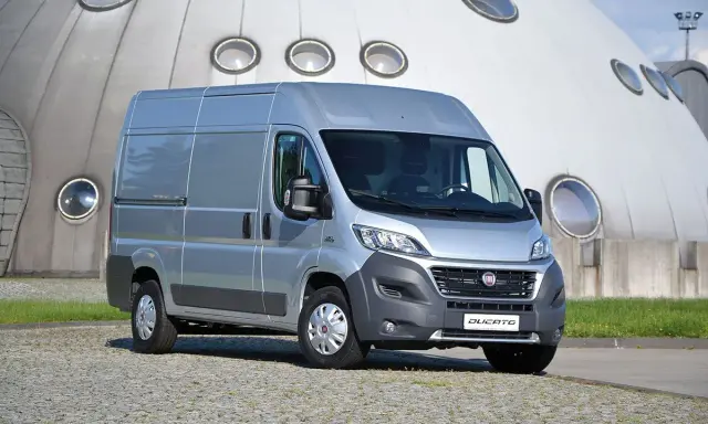 Srebrny Fiat Ducato 2.3 Multijet zaparkowany przed futurystycznym budynkiem z okrągłymi oknami.