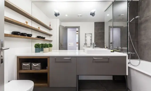 Moderno baño con ducha, bañera y lavabo sobre mueble gris. Estanterías de madera con cuencos negros. Un ejemplo de presupuesto de reforma de baño.