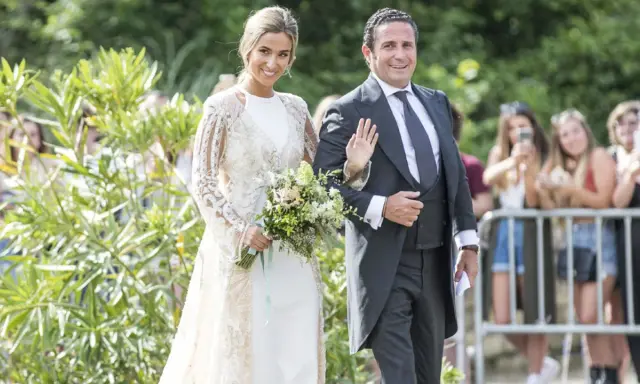 Novia y novio sonríen en la boda de María Pombo. Ella lleva un vestido blanco con encaje y él un traje gris.
