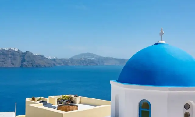 Blaue Kuppel einer Kirche in Oia, Santorini, mit Blick auf das tiefblaue Meer und die zerklüftete Küste.
