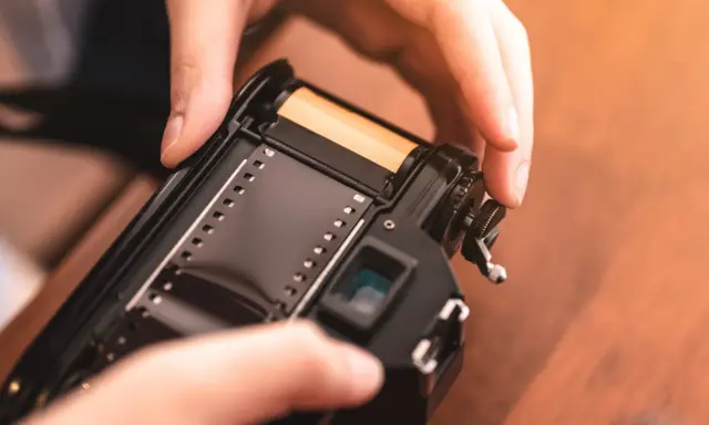 Manos insertando rollo de película en cámara analógica, un paso clave para aprender como revelar fotos en casa.