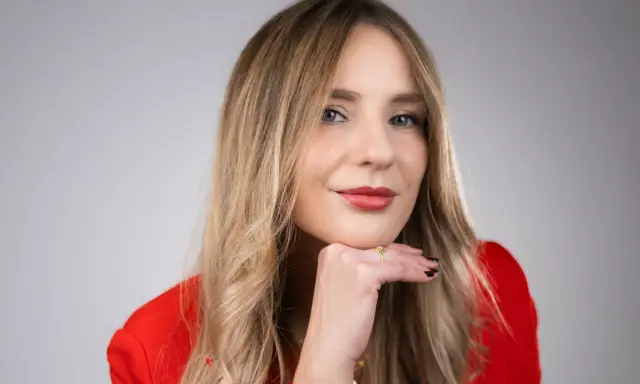 Francesca Florio, con un blazer rosso, appoggia il mento sulla mano, un sorriso pensieroso.