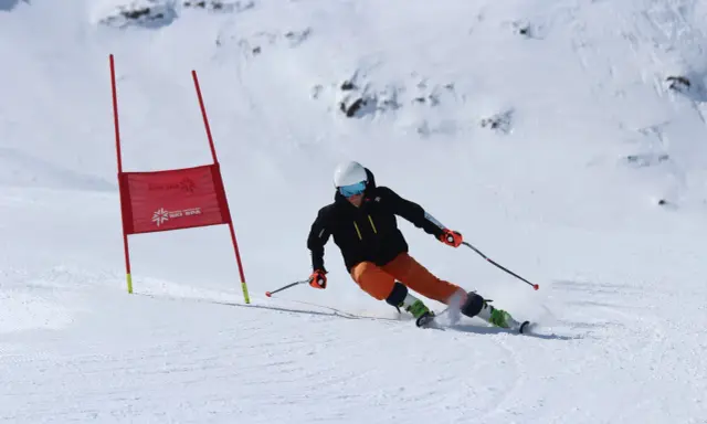 Narciarka na trasie slalomu, w kasku i goglach, dynamicznie pokonuje zakręt, wzbijając śnieg.