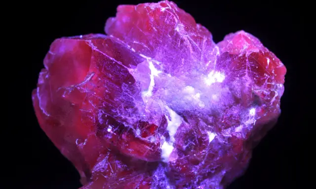 Cristallo rosso intenso, illuminato da luce viola, che fa pensare a qual è la pietra più preziosa al mondo.