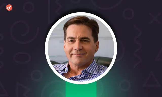 Uśmiechnięty Craig Wright w niebiesko-białej koszuli w kratę, z kluczem w lewym górnym rogu.