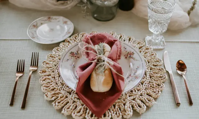 Une table dressée avec élégance, une assiette fleurie, une serviette bordeaux et une **fourchette à la française** en cuivre, prête pour un repas raffiné.