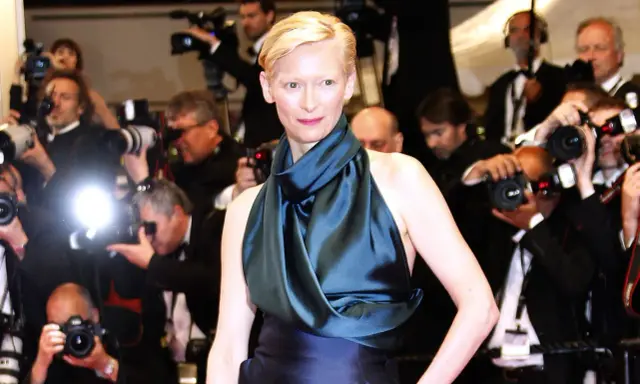 Tilda Swinton poses on the red carpet, surrounded by flashing cameras and eager photographers.