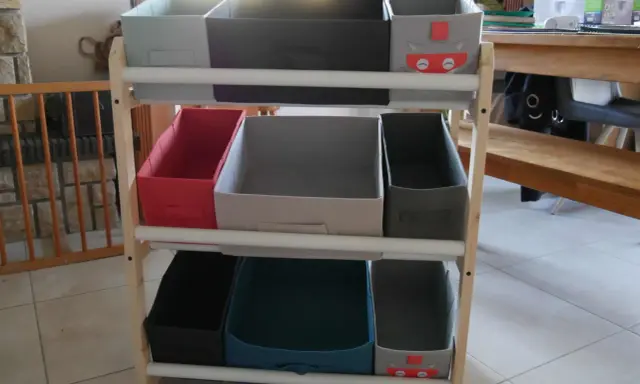 Étagère en bois avec des bacs de rangement pour jouets, dont un décoré d'un chat super-héros. Idéal pour fabriquer un rangement jouet organisé.