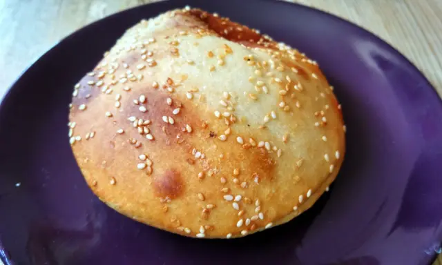 Bułka do hamburgerów posypana sezamem na fioletowym talerzu.