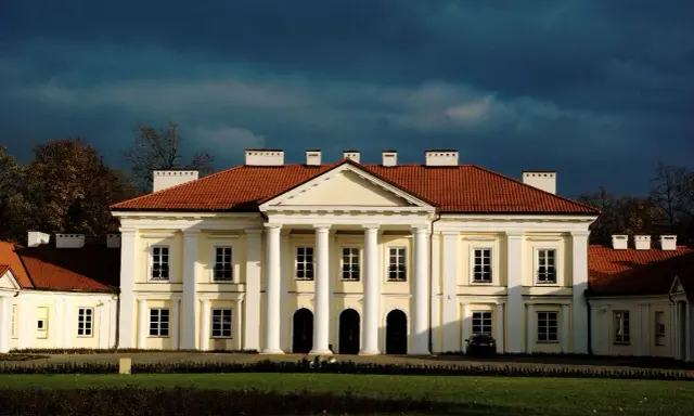 Pałac w Siedlcach, jedna z głównych atrakcji miasta, z charakterystycznym portykiem i czerwonym dachem, na tle burzowego nieba.