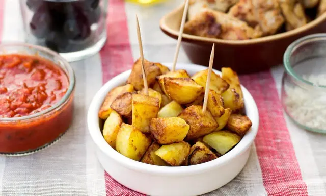Patatas bravas dorées, servies avec une sauce tomate épicée et des olives. Un délice pour l'apéro !