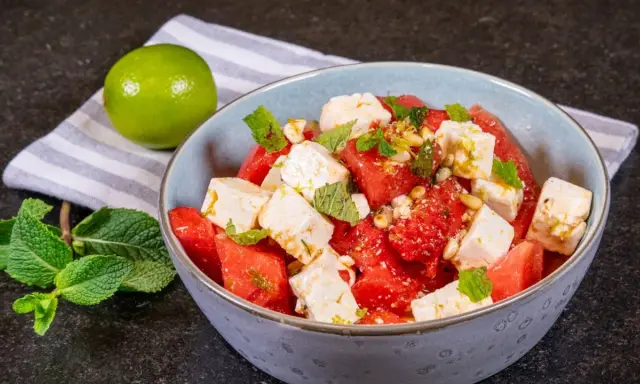 Erfrischender Wassermelonen-Feta-Salat mit Minze und Pinienkernen, garniert mit Limettenabrieb. Perfekt für heiße Tage.