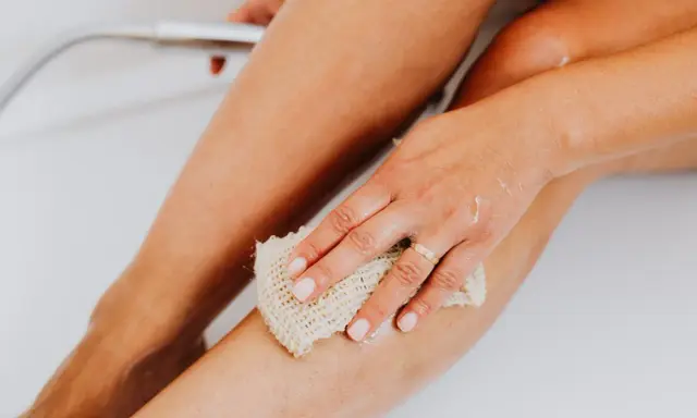 Une main utilise un gant de toilette pour exfolier sa peau, révélant une peau douce et lisse. C'est une étape clé pour savoir comment exfolier sa peau.