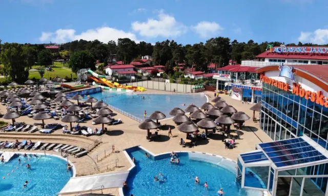 Słoneczny aquapark nad morzem z basenami, zjeżdżalniami i leżakami pod parasolami.