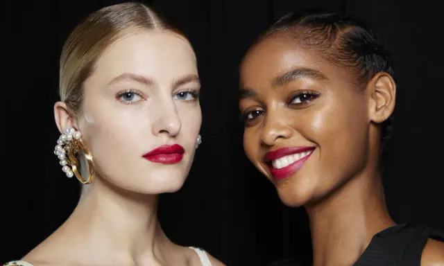 Dos modelos lucen un maquillaje para boda con labios rojos vibrantes y piel radiante. Una lleva un pendiente de perlas, la otra sonríe.