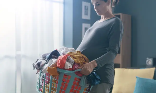 Ciężarna kobieta z koszem prania. Dźwiganie w ciąży bywa wyzwaniem, ale ona radzi sobie z codziennymi obowiązkami.