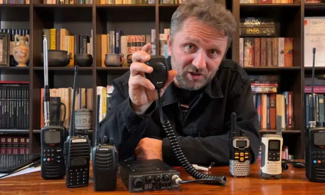Mężczyzna prezentuje sprzęt CB radio, pokazując różne modele i akcesoria, które wpływają na zasięg.
