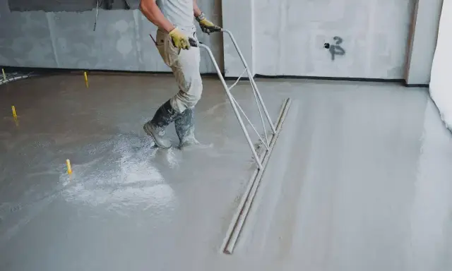 Robotnik wyrównuje świeżą wylewkę betonową na zewnątrz, dbając o odpowiednią minimalną grubość.