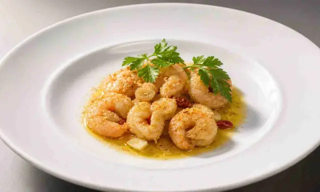 Saftige, gebackene Garnelen mit Knoblauch und Petersilie auf einem weißen Teller.