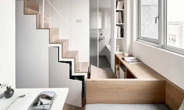 Monolocale con soppalco: scala in legno e bianco, bagno con doccia, scrivania e letto integrati.