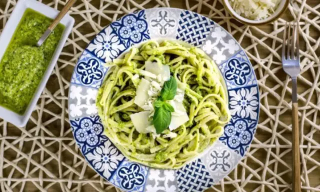 Deliciosa pasta con pesto, ideal para tus recetas de pasta con pesto. Servida en un plato decorado con un toque mediterráneo.