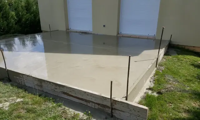Une nouvelle dalle béton fraîchement coulée, prête à sécher. Les coffrages en bois et les fers à béton délimitent la zone.