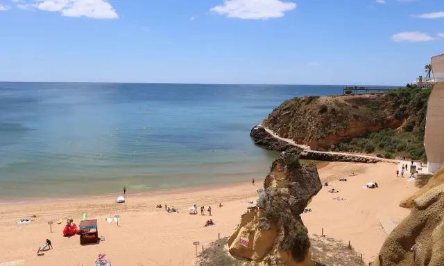 Sonniger Lagos Strand mit goldenem Sand, türkisfarbenem Wasser und Felsformationen. Menschen entspannen sich, spielen und genießen die Aussicht.
