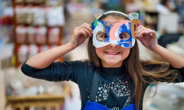 Une jeune fille, le visage caché par un masque coloré, explore la symbolique du visage et la joie de la transformation.
