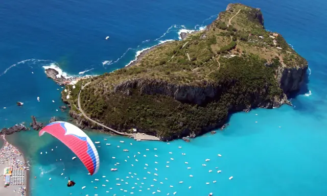 Parapendio su un mare turchese vicino a isole calabresi, con una spiaggia affollata e tante barche.